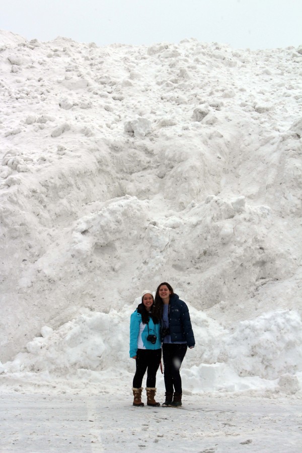 Laura Lynch and Tamyuen Do standing in front of a tower of snow piled up in the parking lot of the Hingham Bathing Beach. 