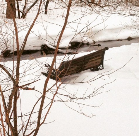 A bench situated on a scenic stream in Hingham, almost covered in a layer of snow. 