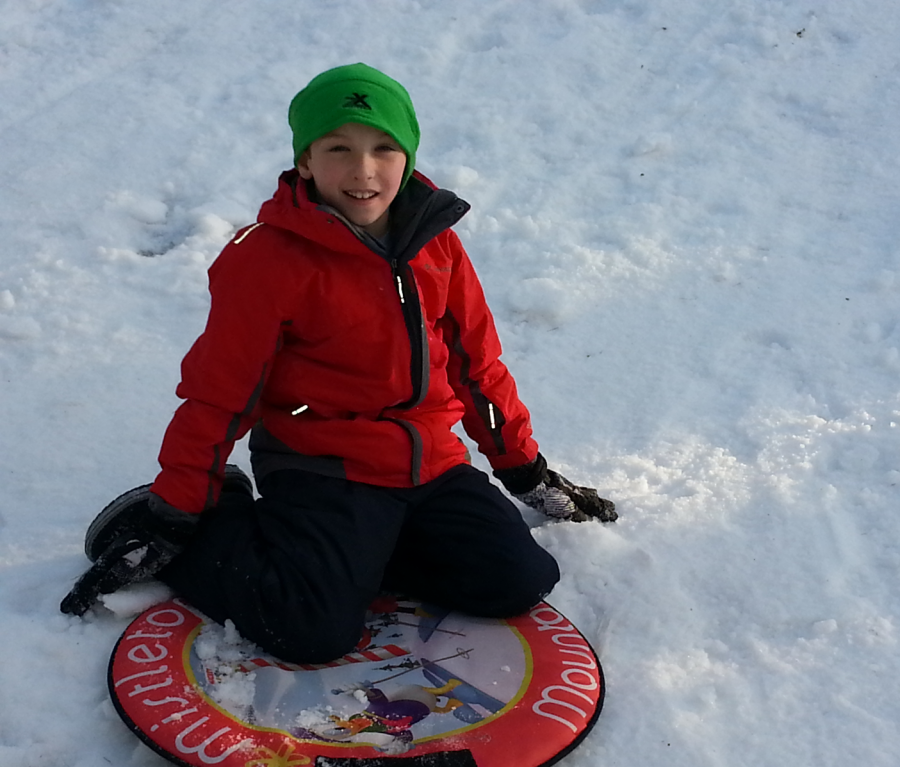 The authors little brother sleds down a snowy slope.