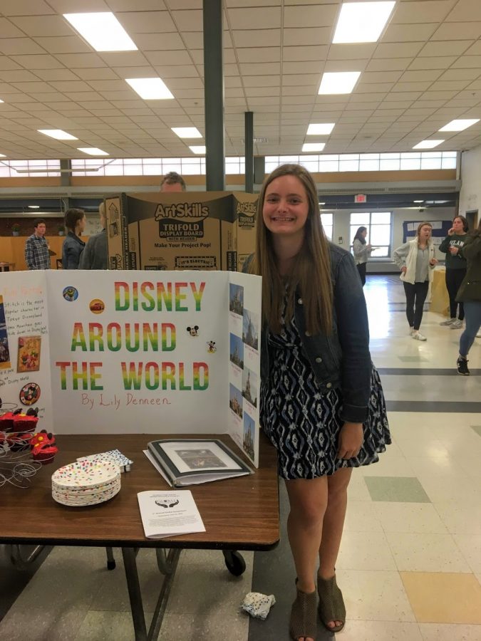 Hingham High School Alumna and former Global Citizenship Program member Lily Deneen stands next to her Disney Around the World portfolio project that gained her a Global Competency Certificate. 