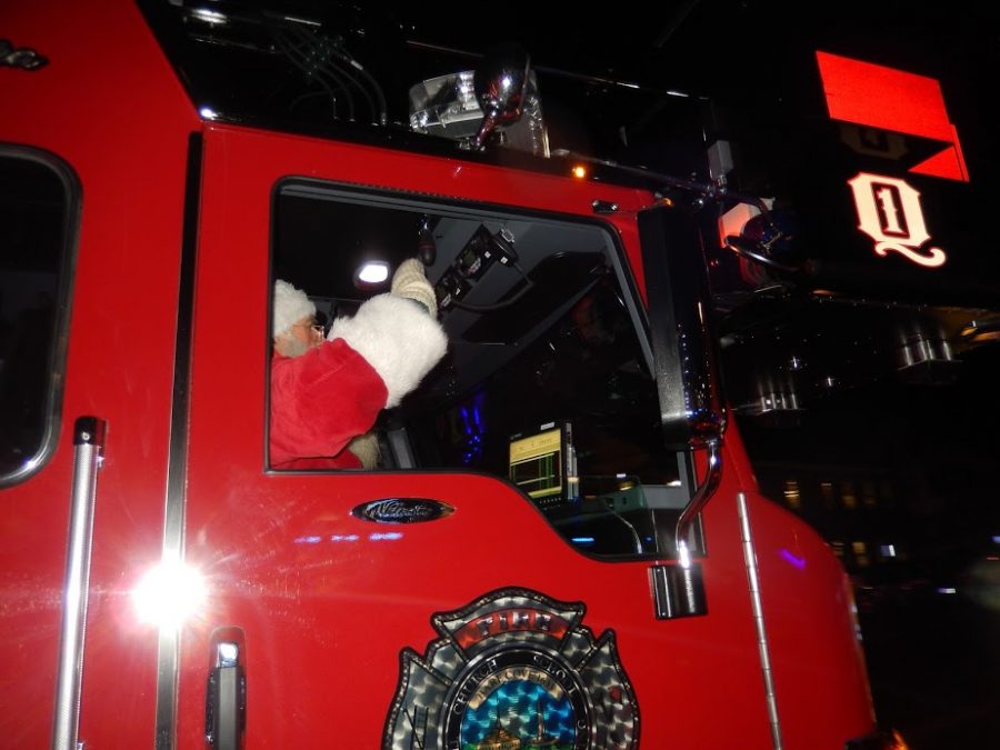 Santa rides into the square in the front seat of a fire truck. 