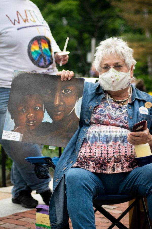 A woman holds up her beautiful painting of a Black Mother and child.