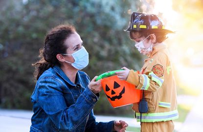 A parent helps her young firefighter with his candy bag on Halloween while following COVID-19 protocol in masks.