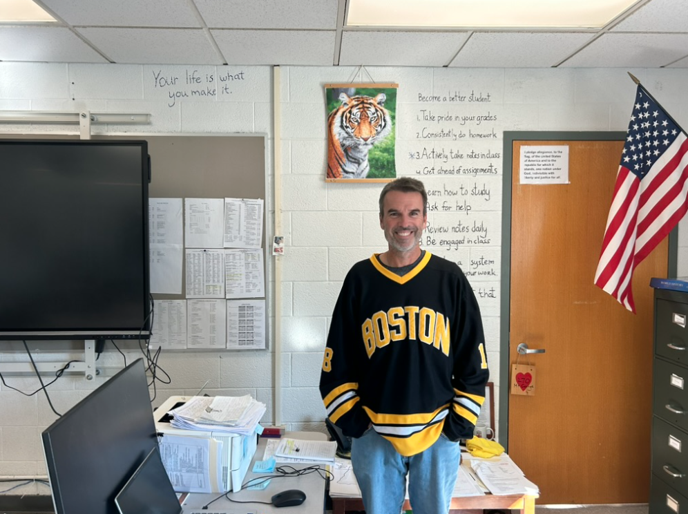 Mr. George, repping his Bruins gear for Jersey Day, poses at his desk in front of the tiger poster.