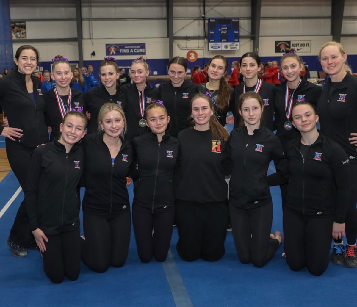 Hingham gymnasts and coaches pose for a team photo at league championships. 
Top row (left to right): Coach Boyd, Grace Whiting, Avery Erik, Amelia Murgatroyd, Erin Murray, Ayra Rizvanbegovic, Vivien Nicholas, Jessica Scipione, and Coach Hennessy. Bottom row (left to right): Grace Zimmerman, Ciara O’Connor, Phoebe Hertzog, Leah Frady (captain), Lillian Hamilton, and Charlotte Passeggio. Not pictured: captain Ava Pappone.